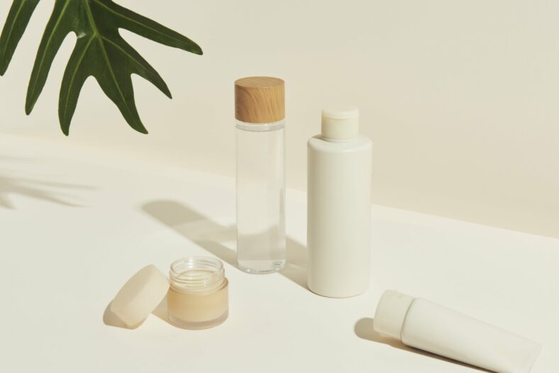 koerperpflegeprodukte.jpg Verschiedene kosmetische Flaschen und Tiegel, darunter ein Glas mit Holzstoß, auf einem hellen Untergrund.